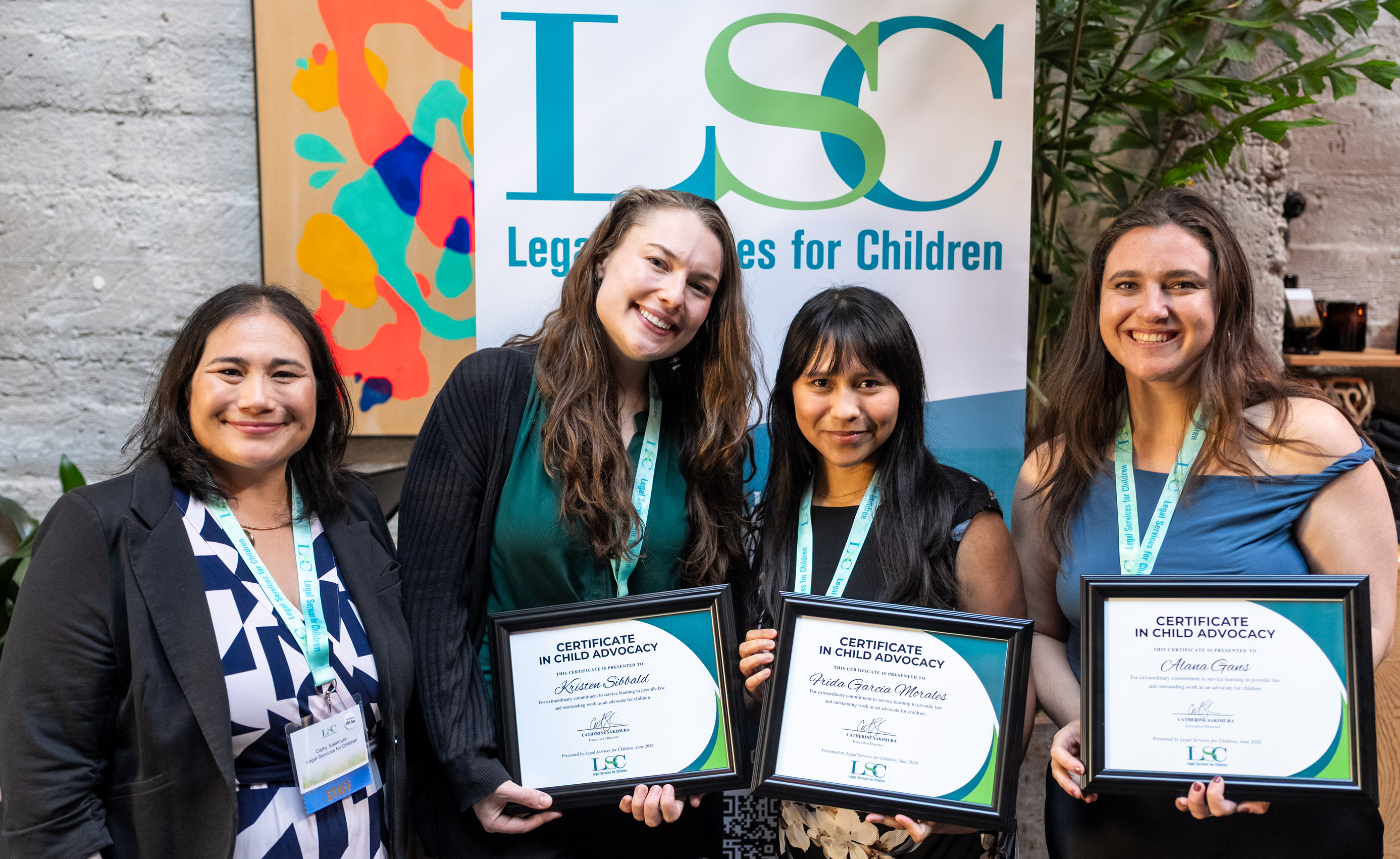 Photo of LSC's 2026 Certificate in Child Advocacy awardees holding their certificates with our Executive Director in front of an LSC banner. From left: LSC Executive Director Cathy Sakimura, awardee Kristen Sibbald, awardee Frida Garcia Morales, and awardee Alana Gans
