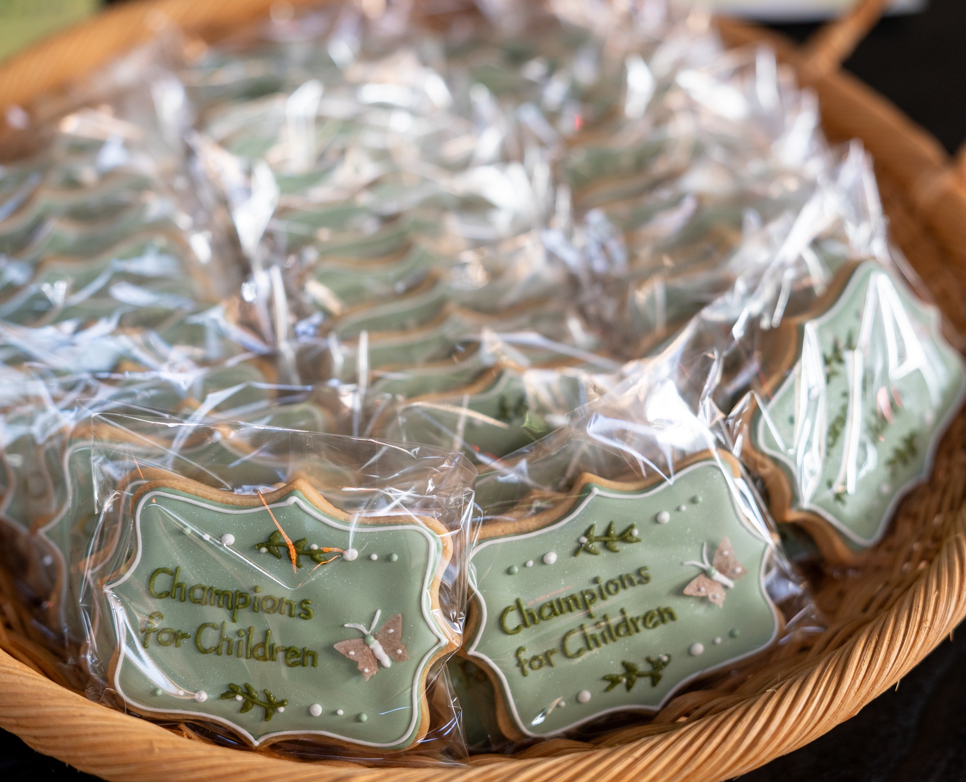 A basket full of sugar cookies decorated with sage green icing, a sugar butterfly, and the text 