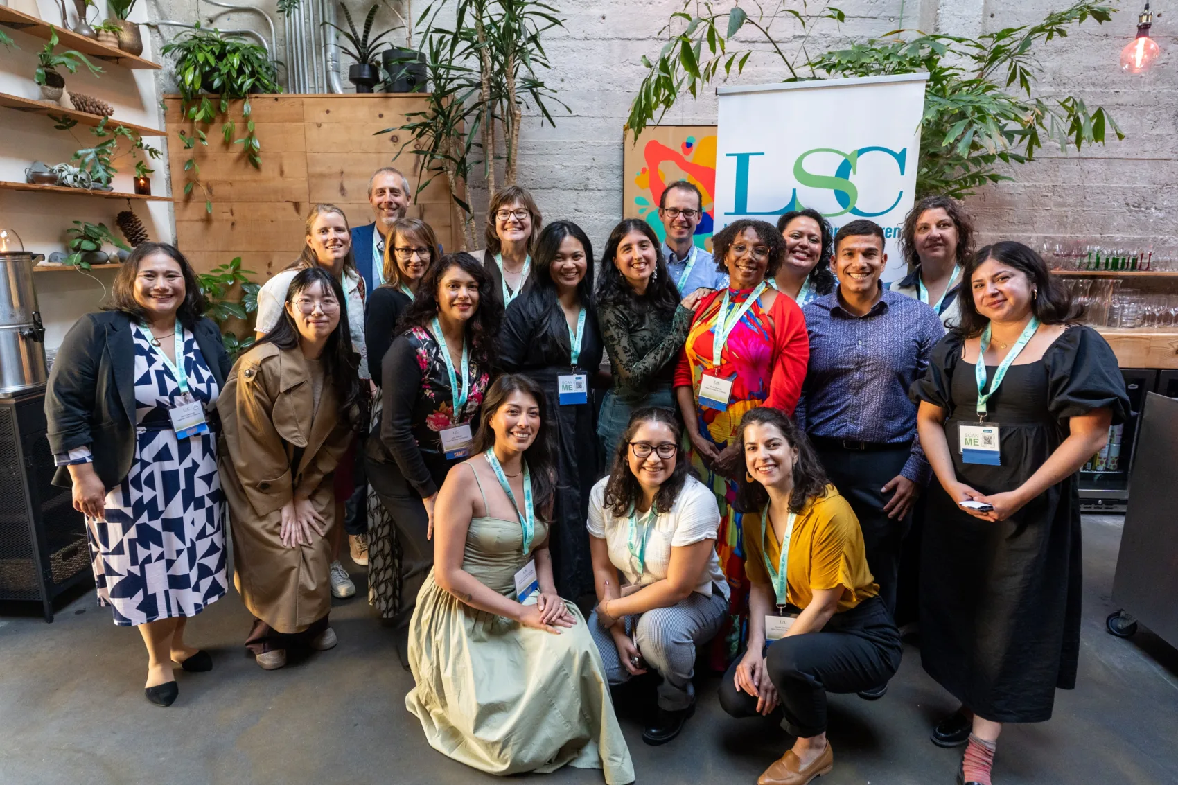 A group of LSC staff gathered in front of an LSC banner and wood walls lined with indoor trees
