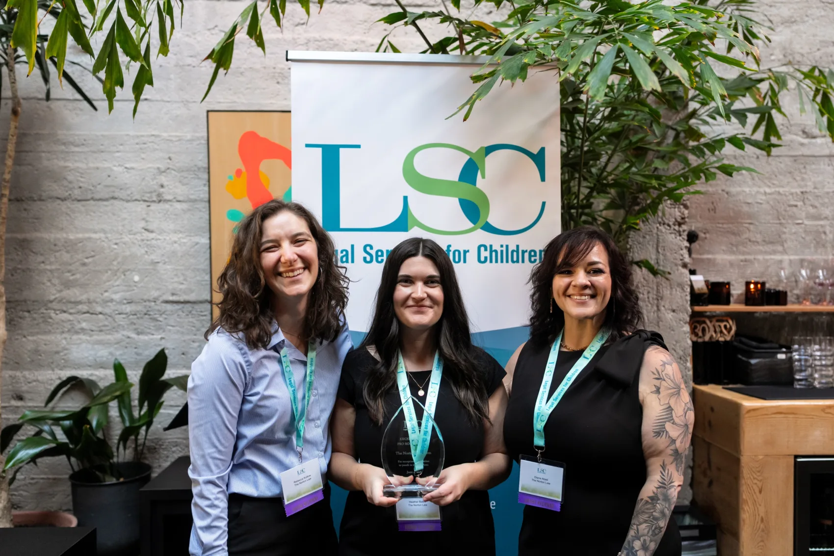 Three 2026 Excellence in Pro Bono awardees with their award, standing in front of an LSC banner