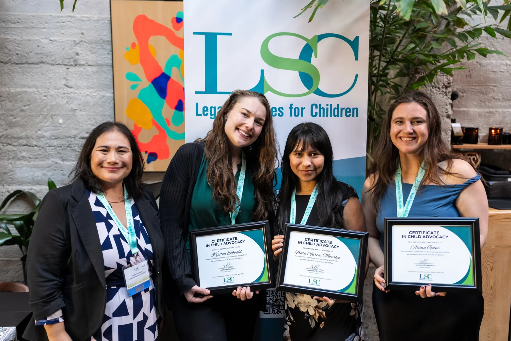 Photo of LSC's 2026 Certificate in Child Advocacy awardees holding their certificates with our Executive Director in front of an LSC banner. From left: LSC Executive Director Cathy Sakimura, awardee Kristen Sibbald, awardee Frida Garcia Morales, and awardee Alana Gans